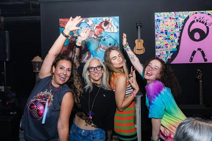 Four women arms up in front of art wall